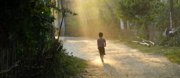 Child walking along a path with sun shining through trees